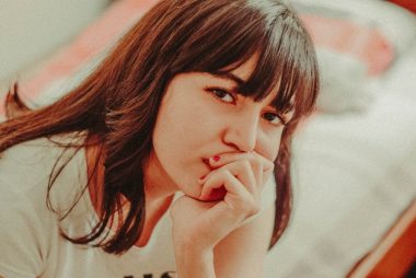 a woman sitting on a bed with her hand on her mouth