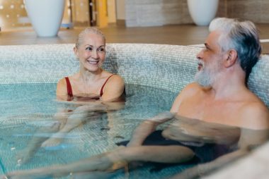 Smiling senior couple relaxing together in an indoor spa pool, enjoying leisure time.